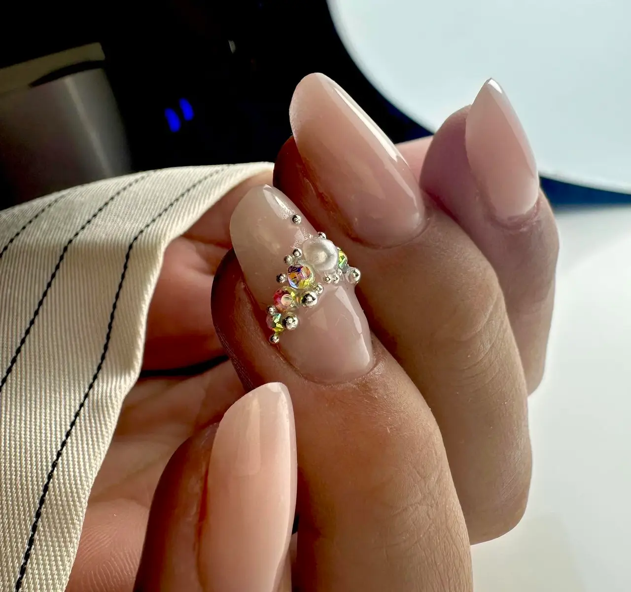 Ongles longs nude en amande, bijou de strass et de perles sur l’annulaire